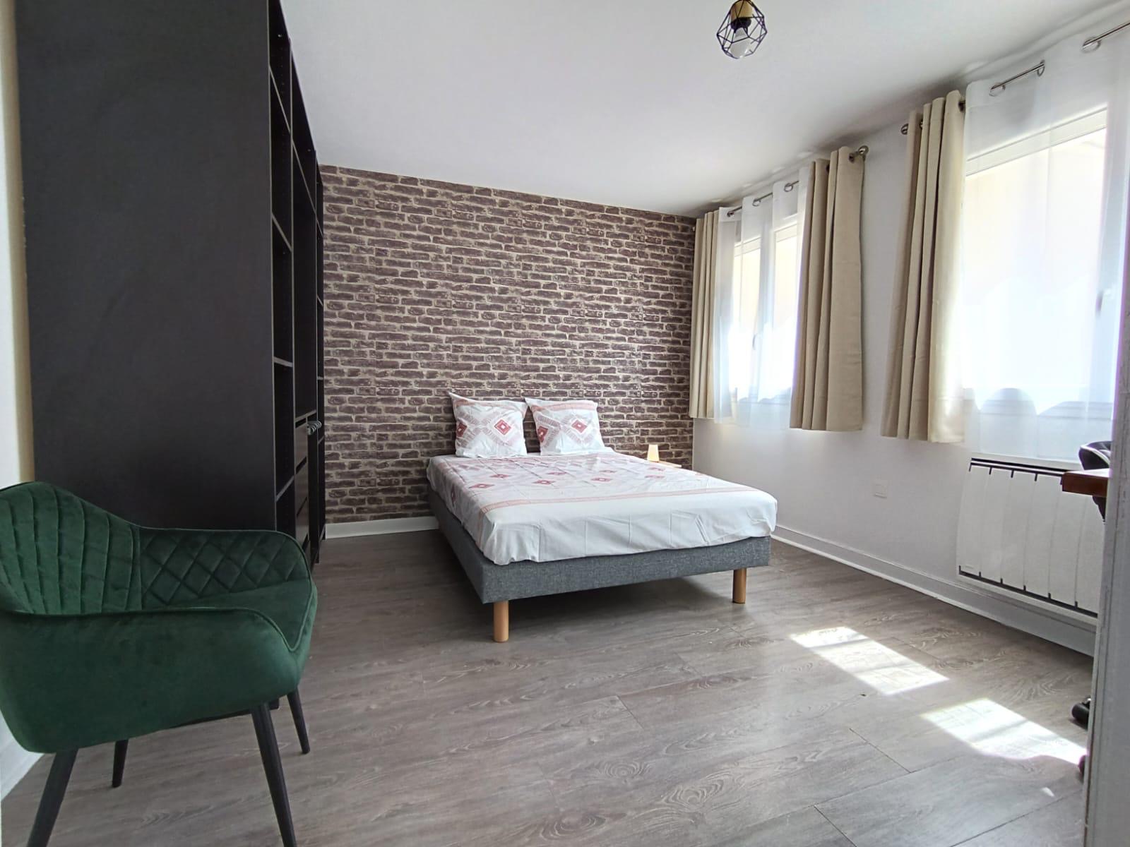 Chambre avec mur en briques, lit double et fauteuil vert